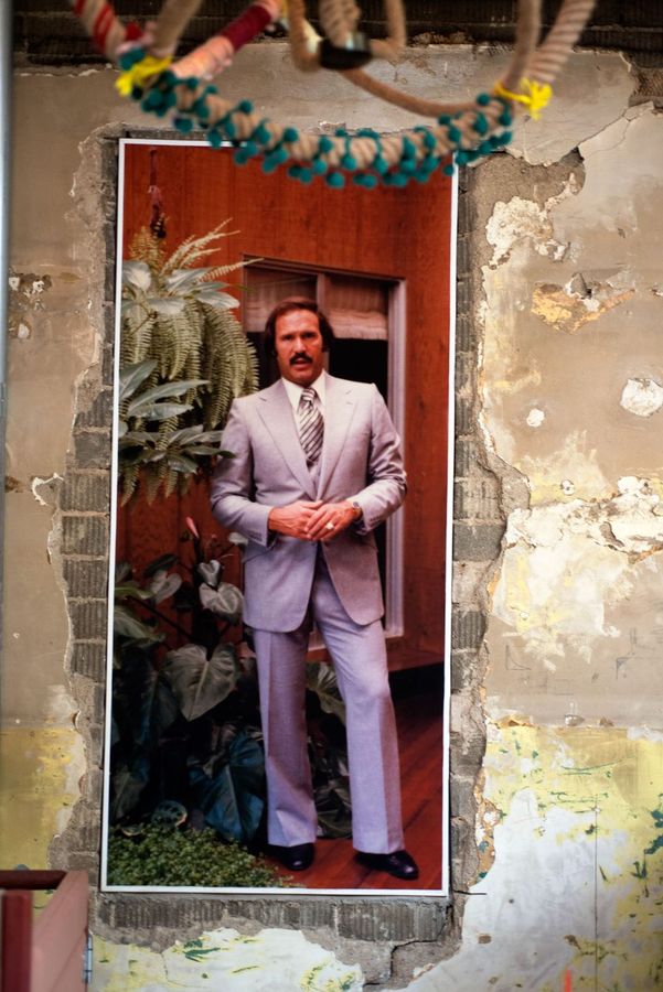 A life-size portrait mural in a pale suit set into a rough plaster wall